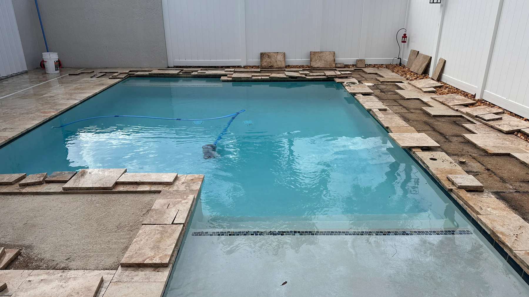 Pool deck pavers lifted and staged around a swimming pool during repair