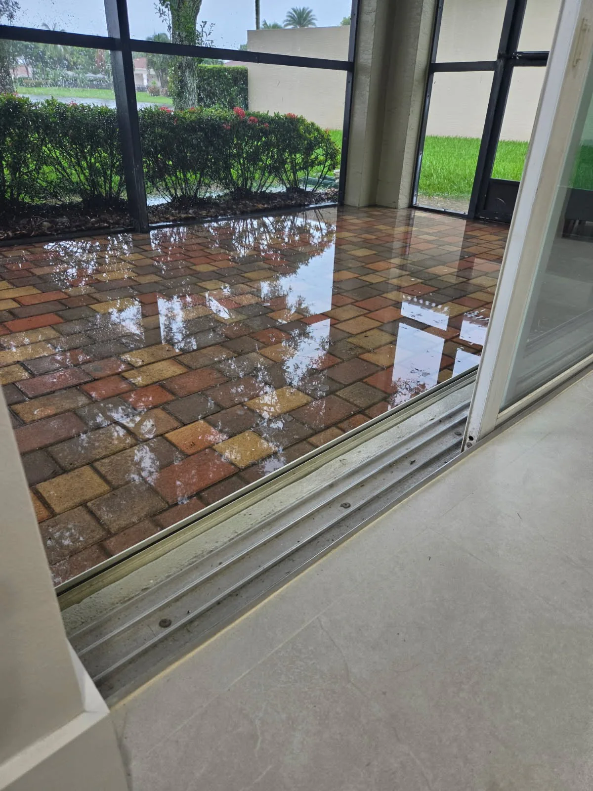 Standing water beside a sliding door on a Delray Beach screened paver patio before repair